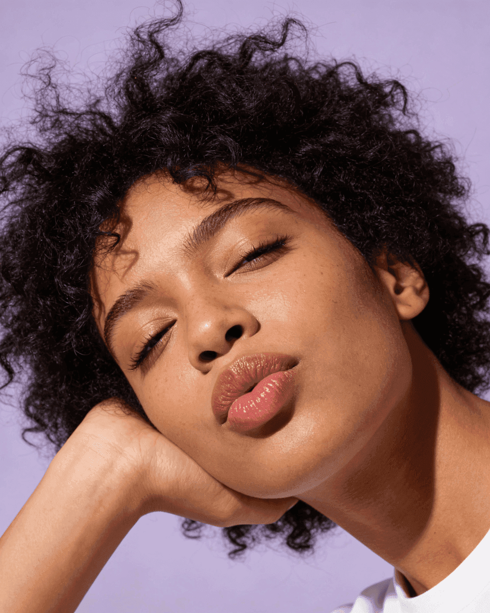 Beauty portrait with glossy lips and voluminous curly hair on lavender background